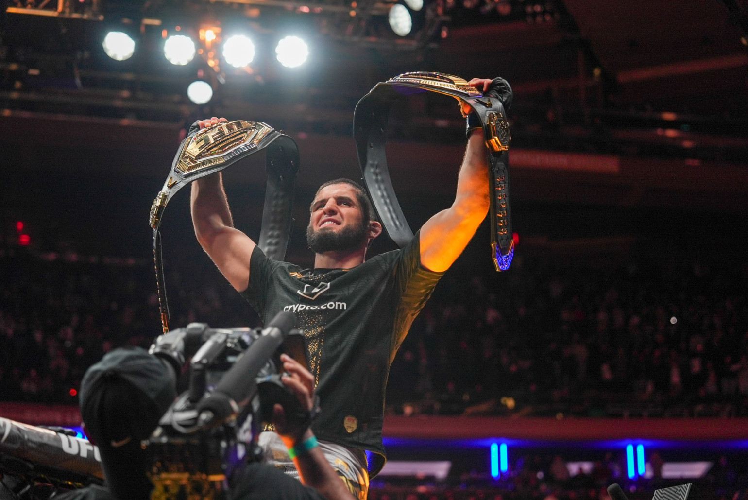 Islam Makhachev celebrating while holding two UFC championship belts